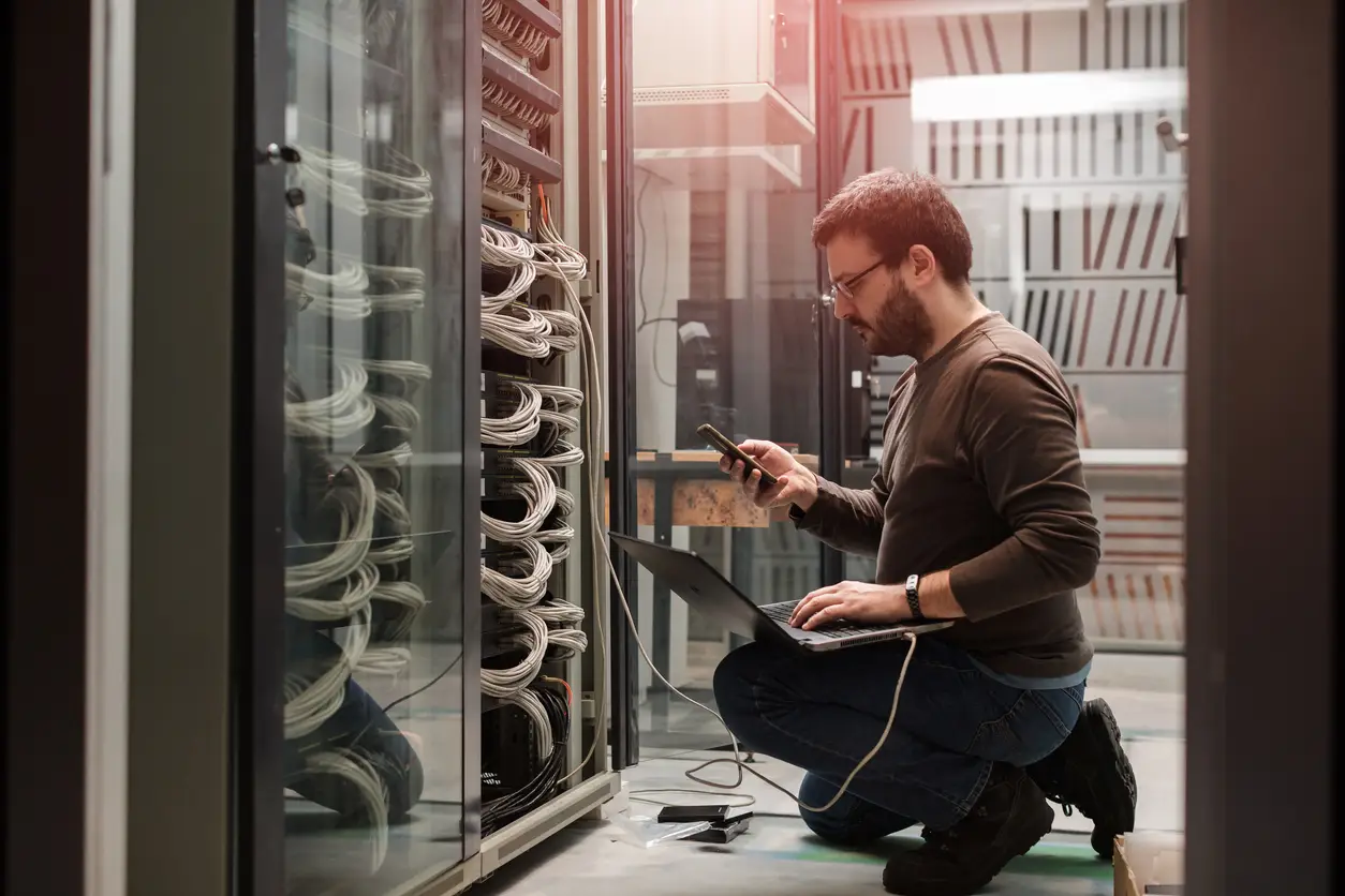 IT professional working on a laptop in a server closet.
