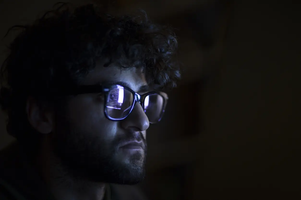 Person with glasses focused on a screen in a dark room.