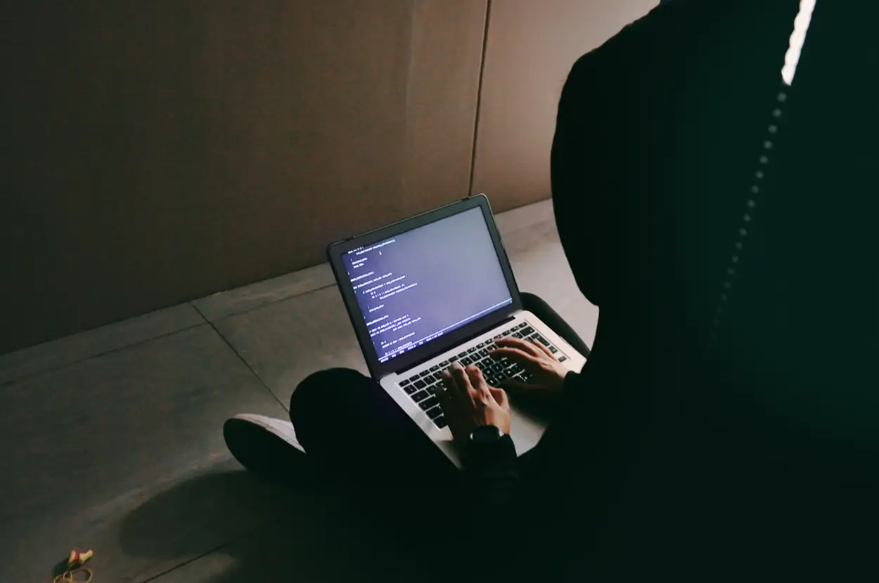 Person coding on a laptop in a dimly lit space, showcasing focus and tech engagement.