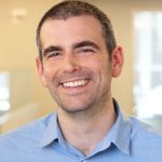 Smiling man in a light blue shirt, showcasing a friendly demeanor in an office setting.