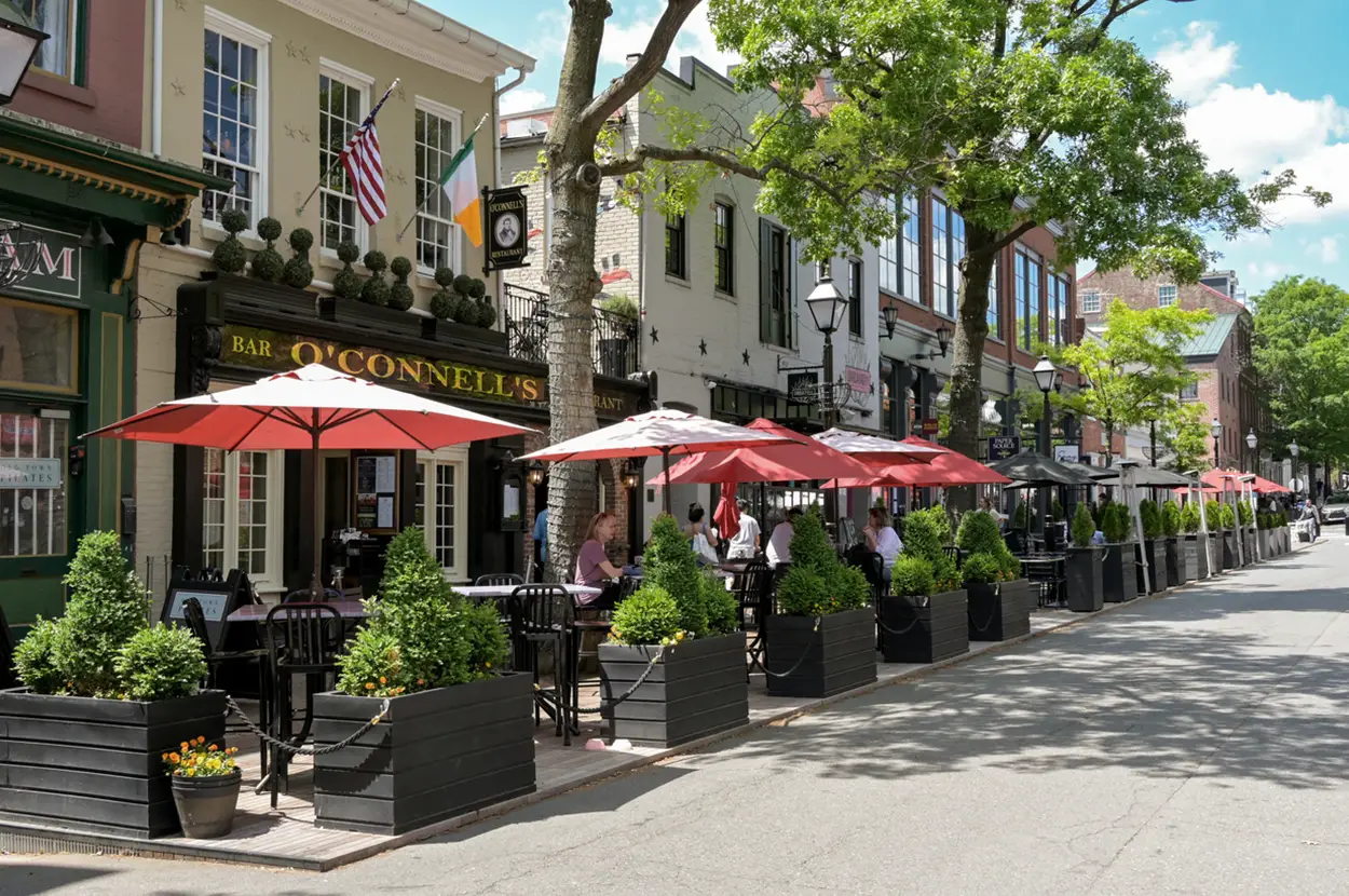 Outdoor dining scene at Bar O'Connell's in Alexandria with umbrellas, greenery, and patrons enjoying a sunny day.