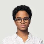 Young woman with curly hair and glasses, wearing a white shirt, against a light gray background.
