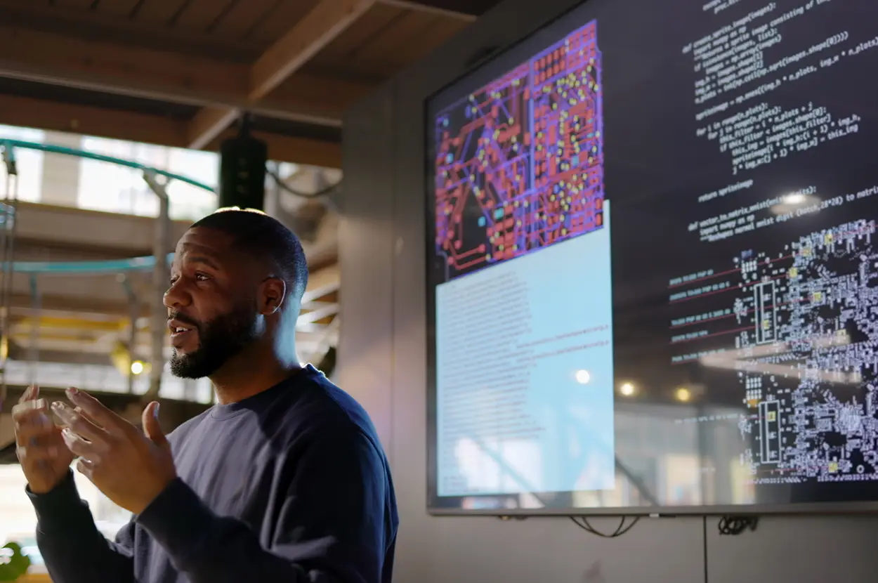 Speaker presenting algorithms on a digital display, showcasing coding and visual patterns in a modern workspace.