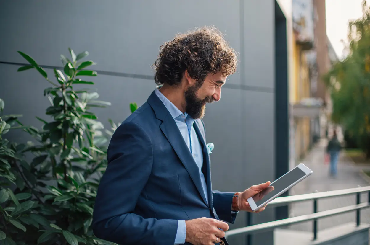 Man in a blue suit reviewing information on a tablet outdoors.