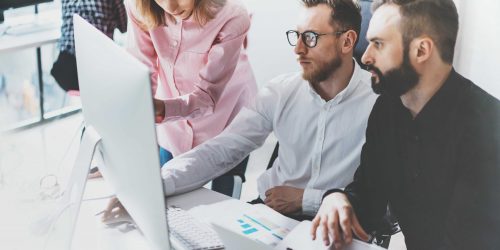 Team collaborating on a project at a modern office, focusing on computer screens and discussing ideas.