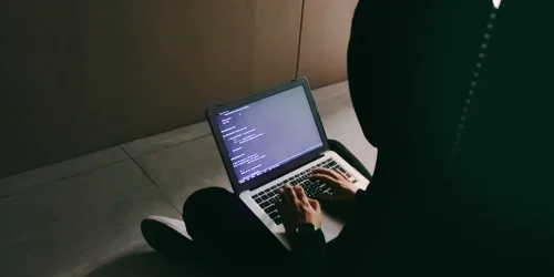 Person coding on a laptop in a dimly lit space, showcasing focus and tech engagement.