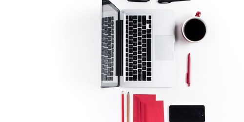 Top view of a workspace featuring a laptop, coffee cup, stationery, and a smartphone on a white background.